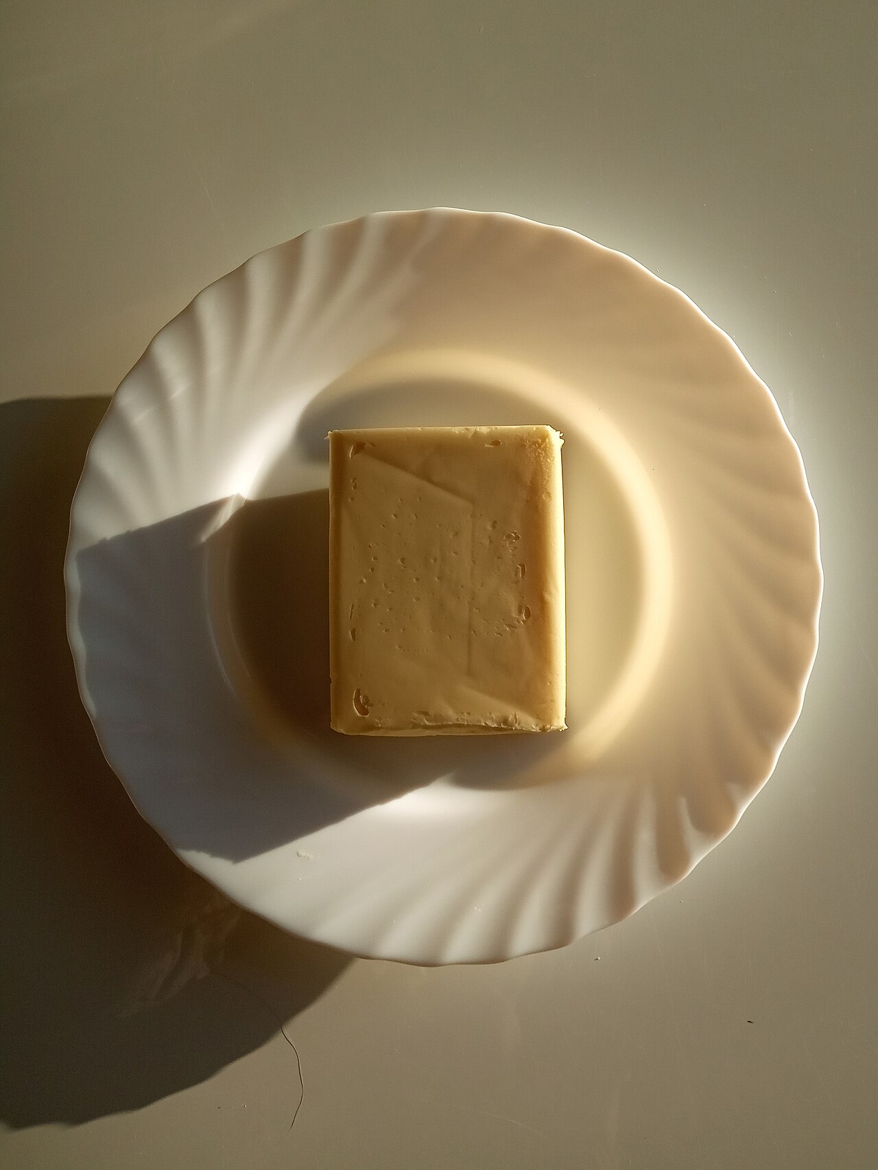 A block of butter on a plate, the end result of churning cream