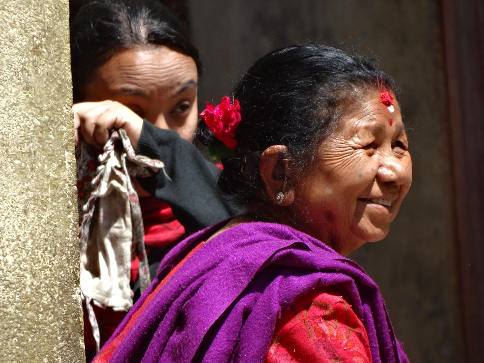 An older woman sits outdoors and looks at the camera.