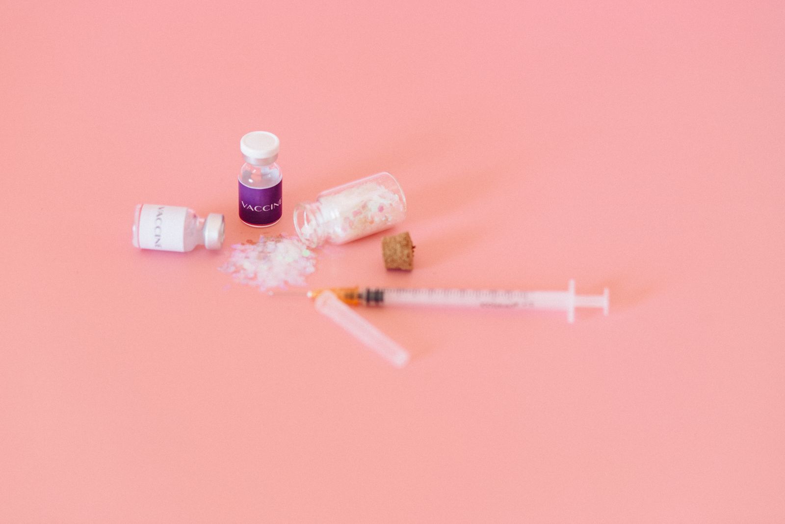 Vaccine vials and a syringe on a soft pink surface