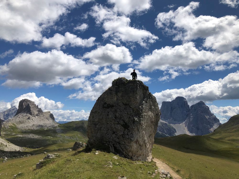 A lone hiker standing on a rock above a mountain trail
