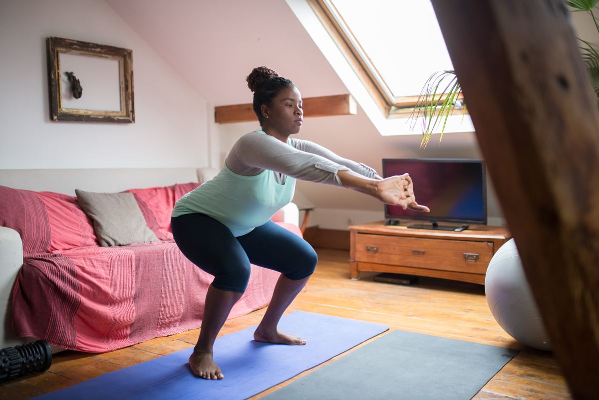 A woman performing squats on a yoga mat in a living room
