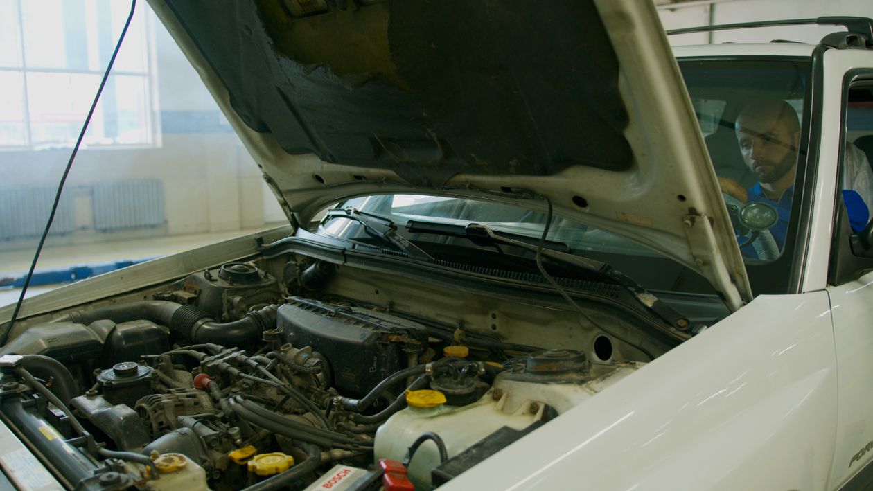 A mechanic checking a car engine under an open hood