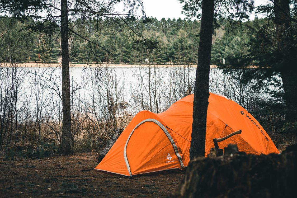 An orange tent pitched near a calm lake surrounded by trees