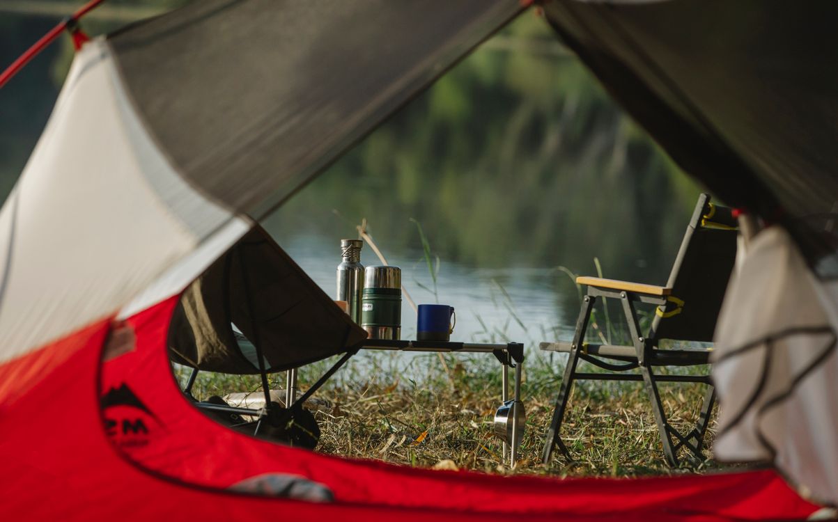 A tent with camping chairs on a river coast, seen from inside another tent