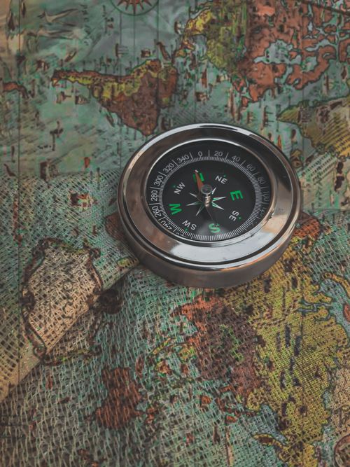 A metal compass rests on a vintage world map, showing old routes and new bearings