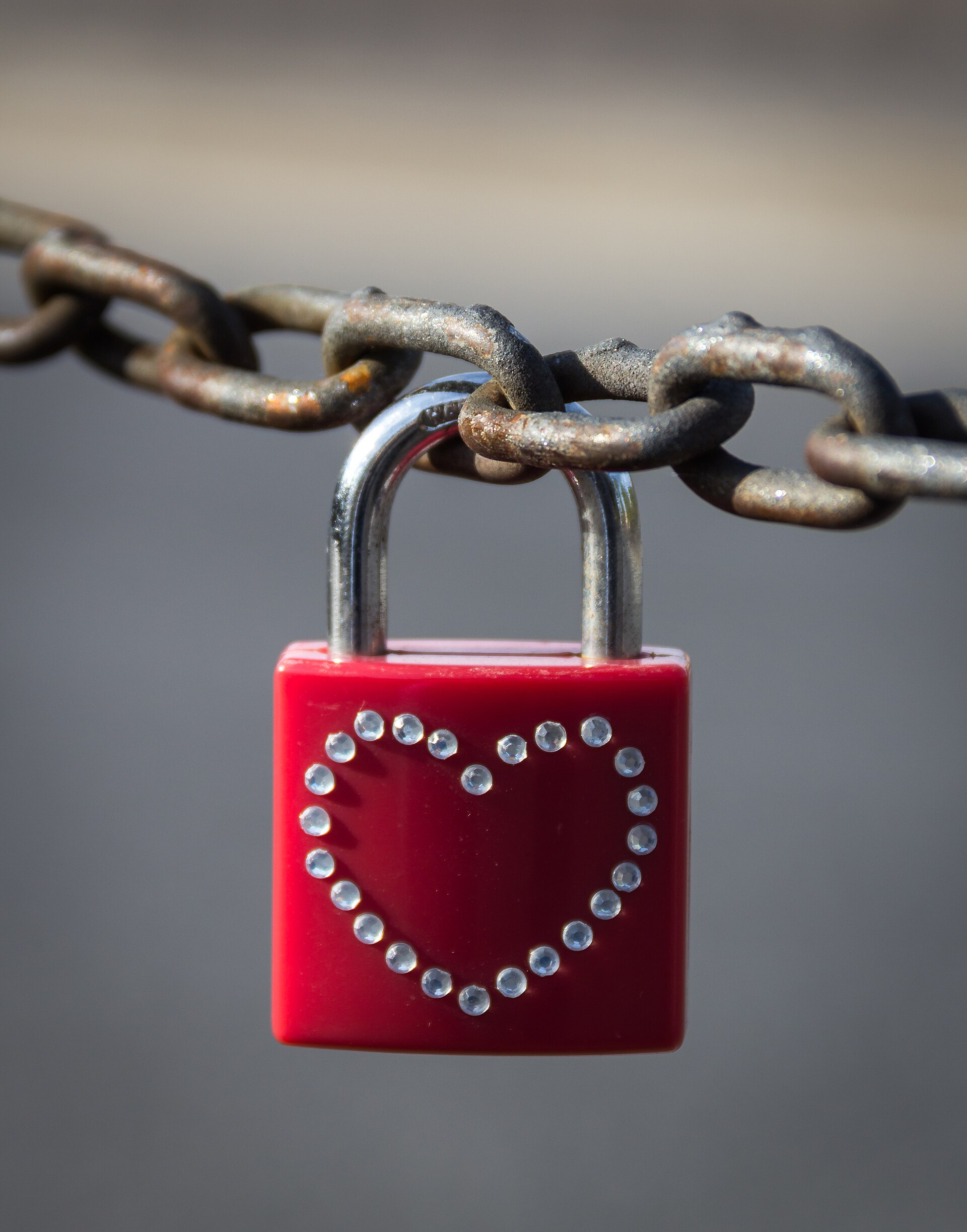 A red padlock with a heart made of small crystals hanging on a metal chain