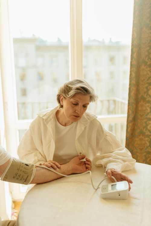 A senior woman checks her blood pressure with a monitor by a window at home