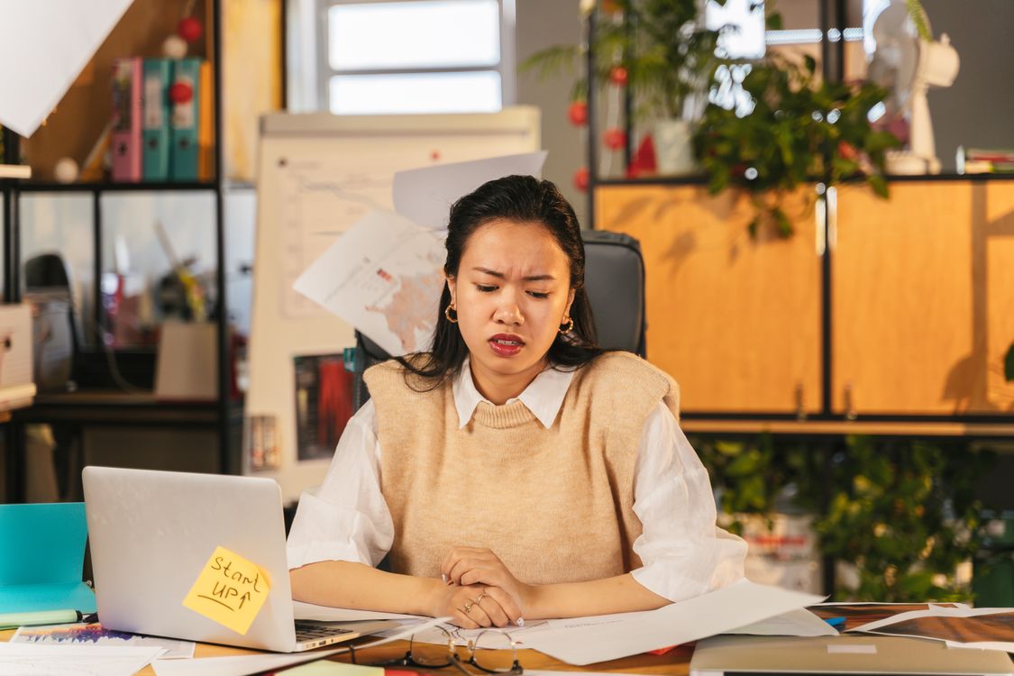 An office worker looking frustrated while sitting at a cluttered desk with a laptop