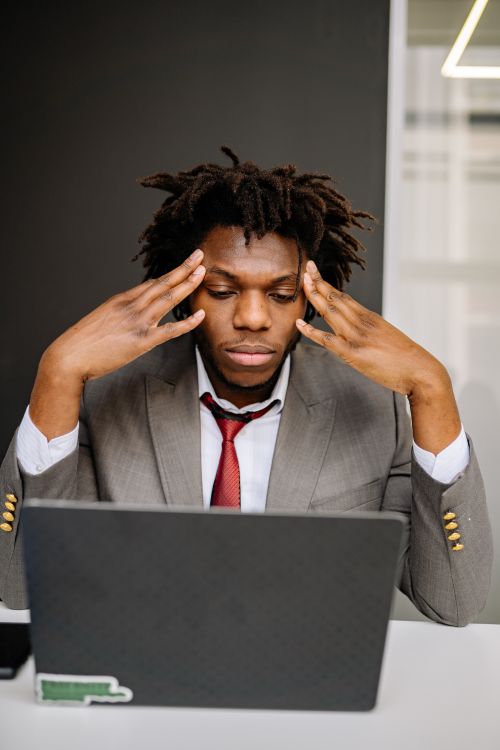 A business professional looking stressed while using a laptop in an office