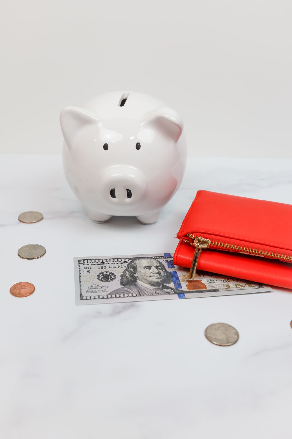 A piggy bank with coins and a red wallet on a desk