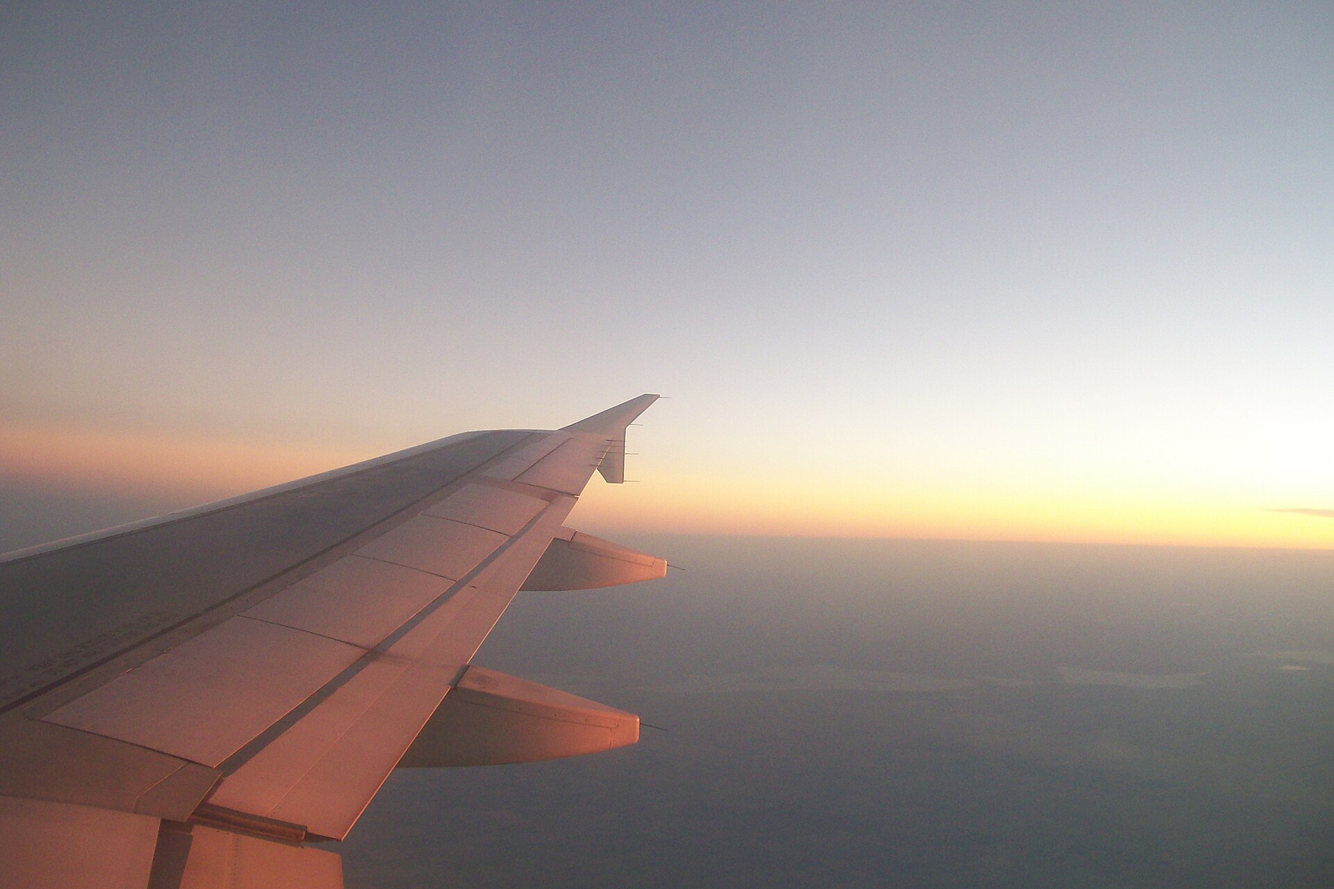 An airplane wing against a sunset sky