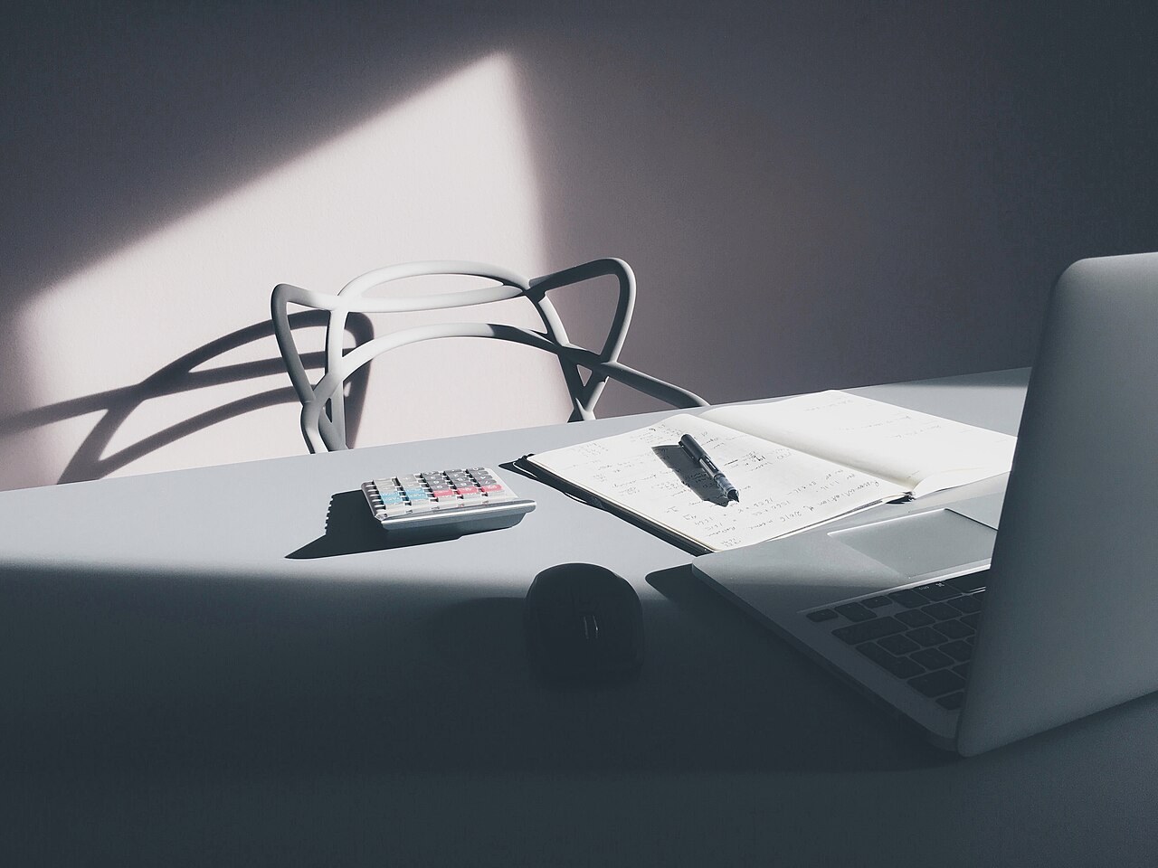 A desk with a calculator, an open notebook, and a laptop