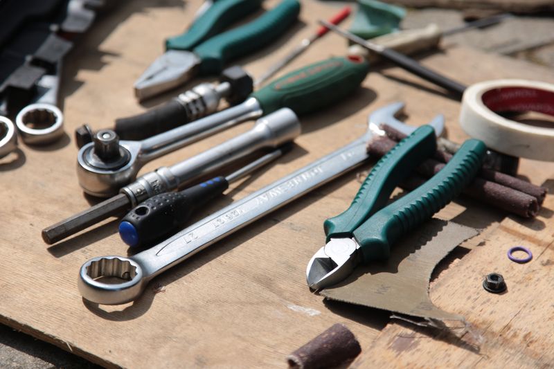 Hand tools including pliers and a wrench on a wooden board