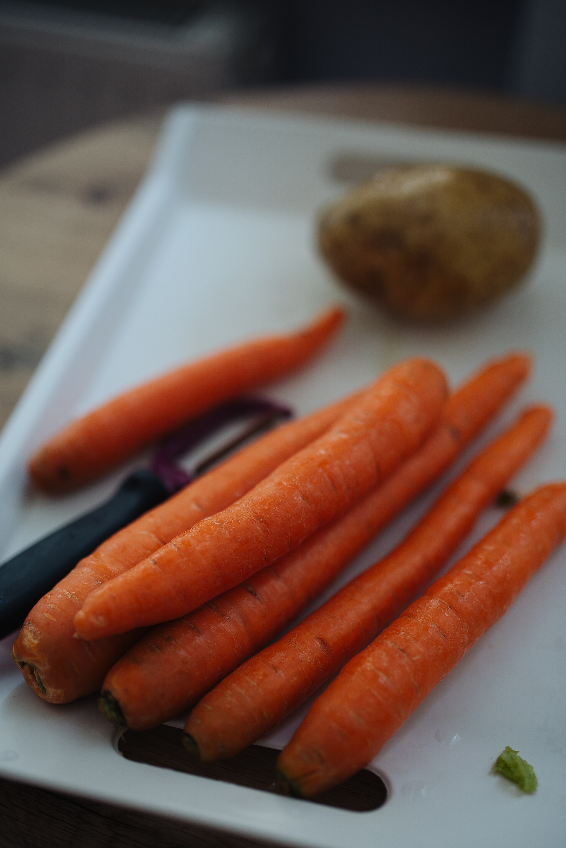 Carrots and a potato on a cutting board beside a knife