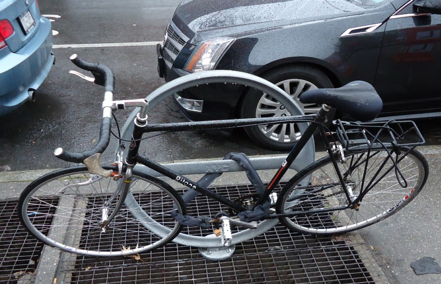 A bicycle locked to a hoop stand on a wet street
