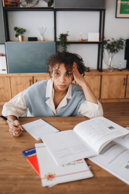 A young woman studying at a desk surrounded by books and notebooks