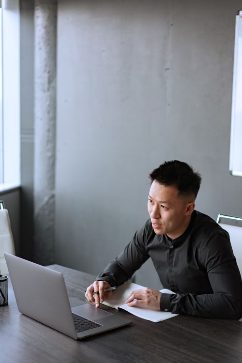 A businessman working on a laptop at a wooden table in an office