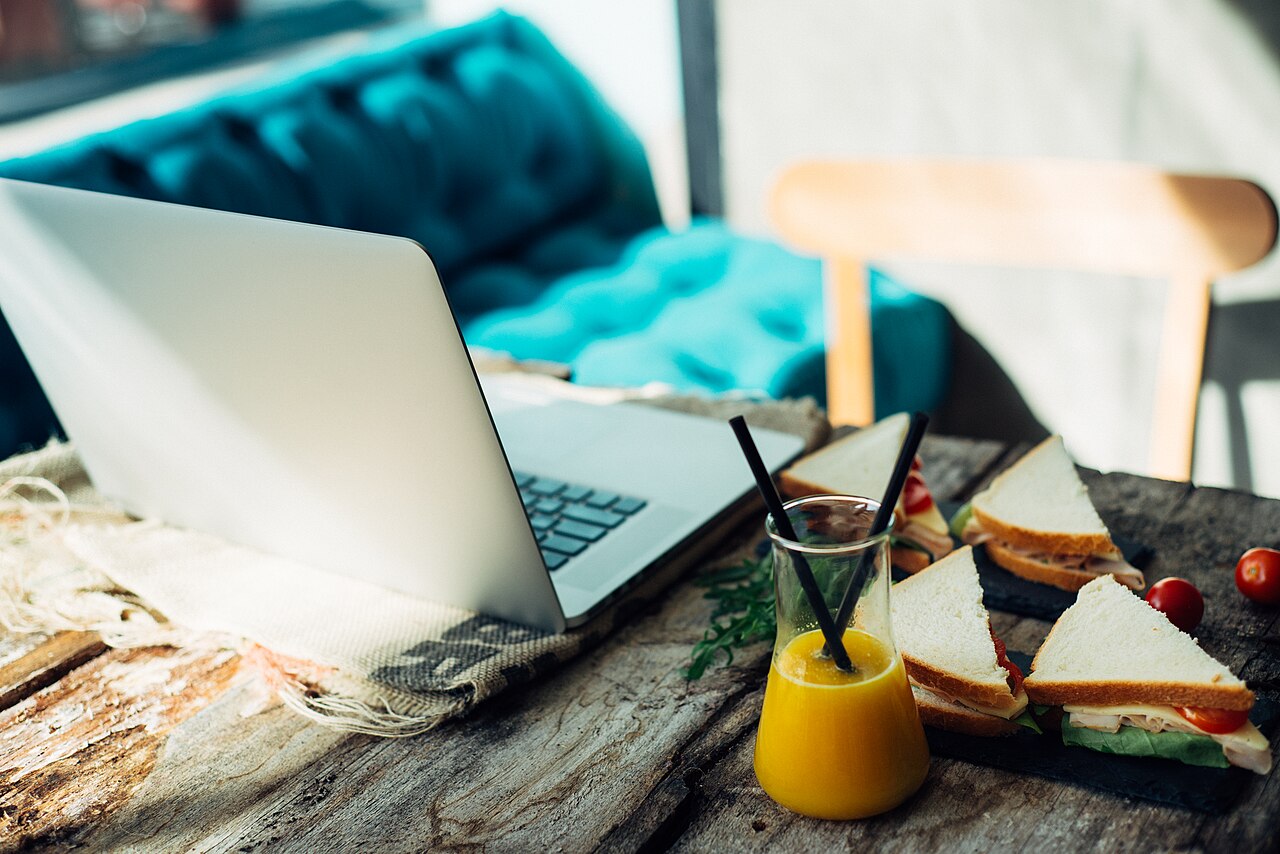 A workspace with a laptop, sandwich, and juice on a wooden table in a cafe