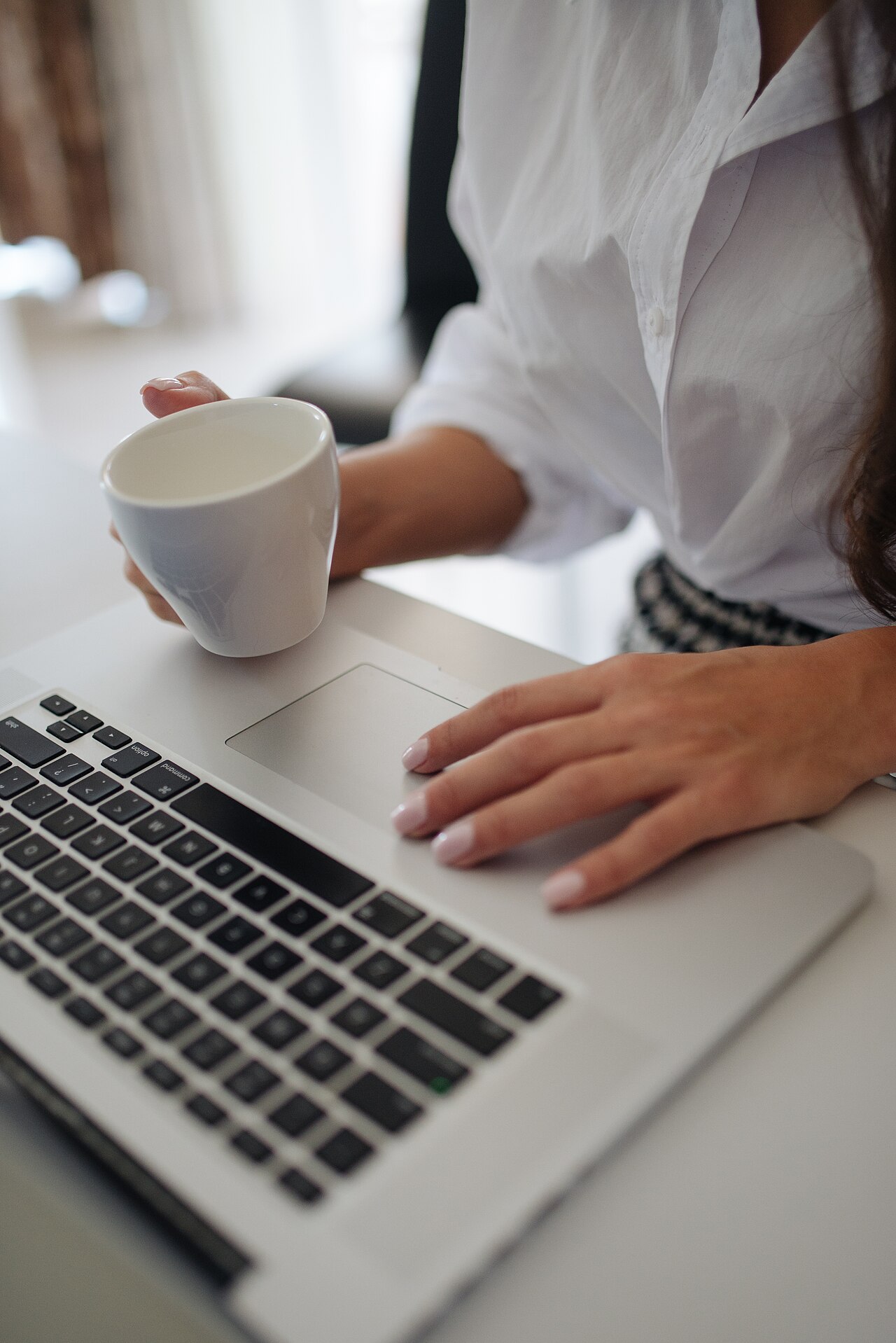 A woman drinks coffee while working on a laptop