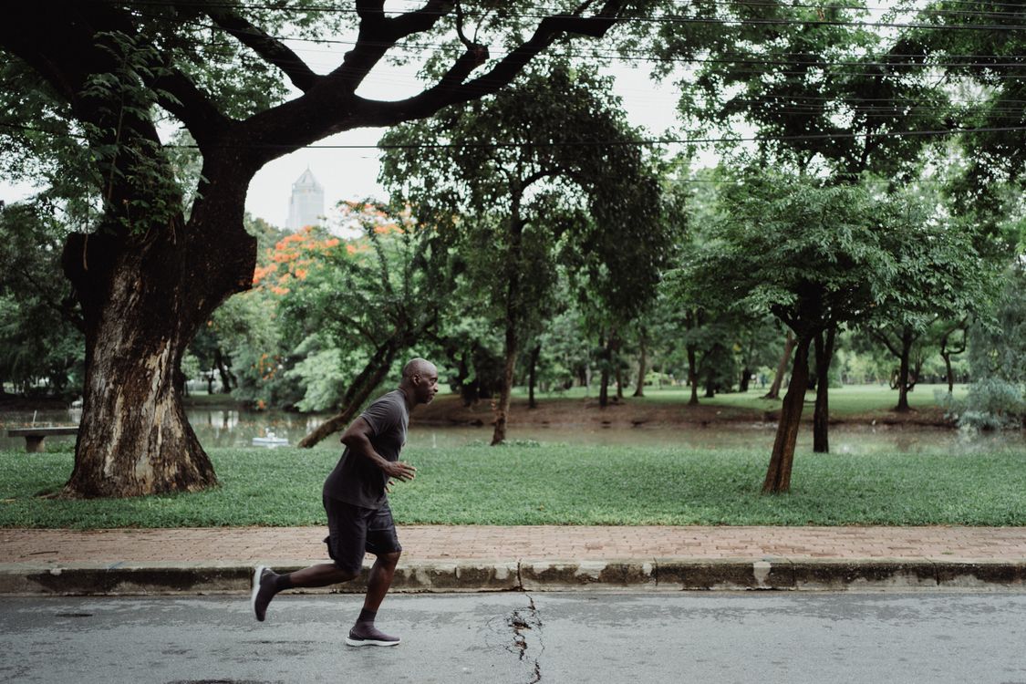 A man jogging in a park with trees and clear skies