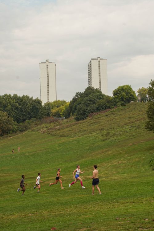 A group of people jogging on a grassy hill in a city park