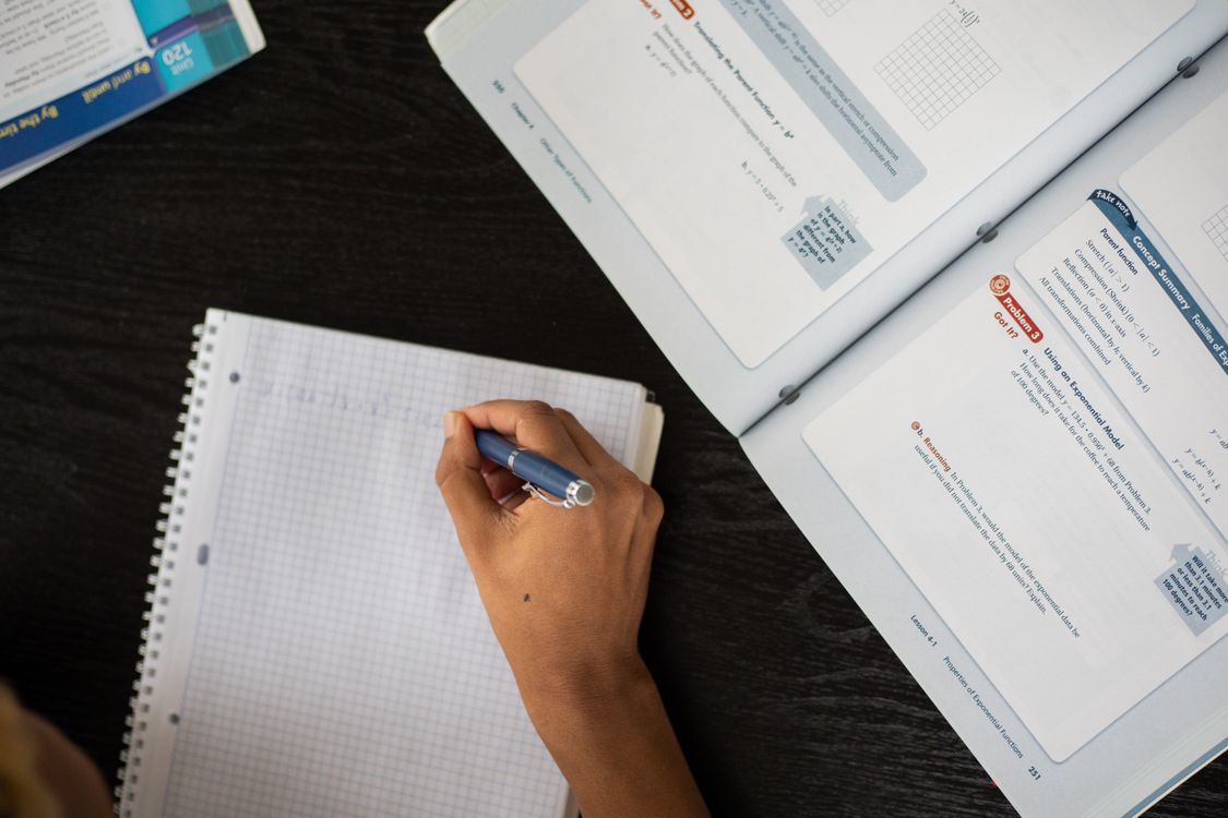 A student writing notes in a notepad with textbooks open