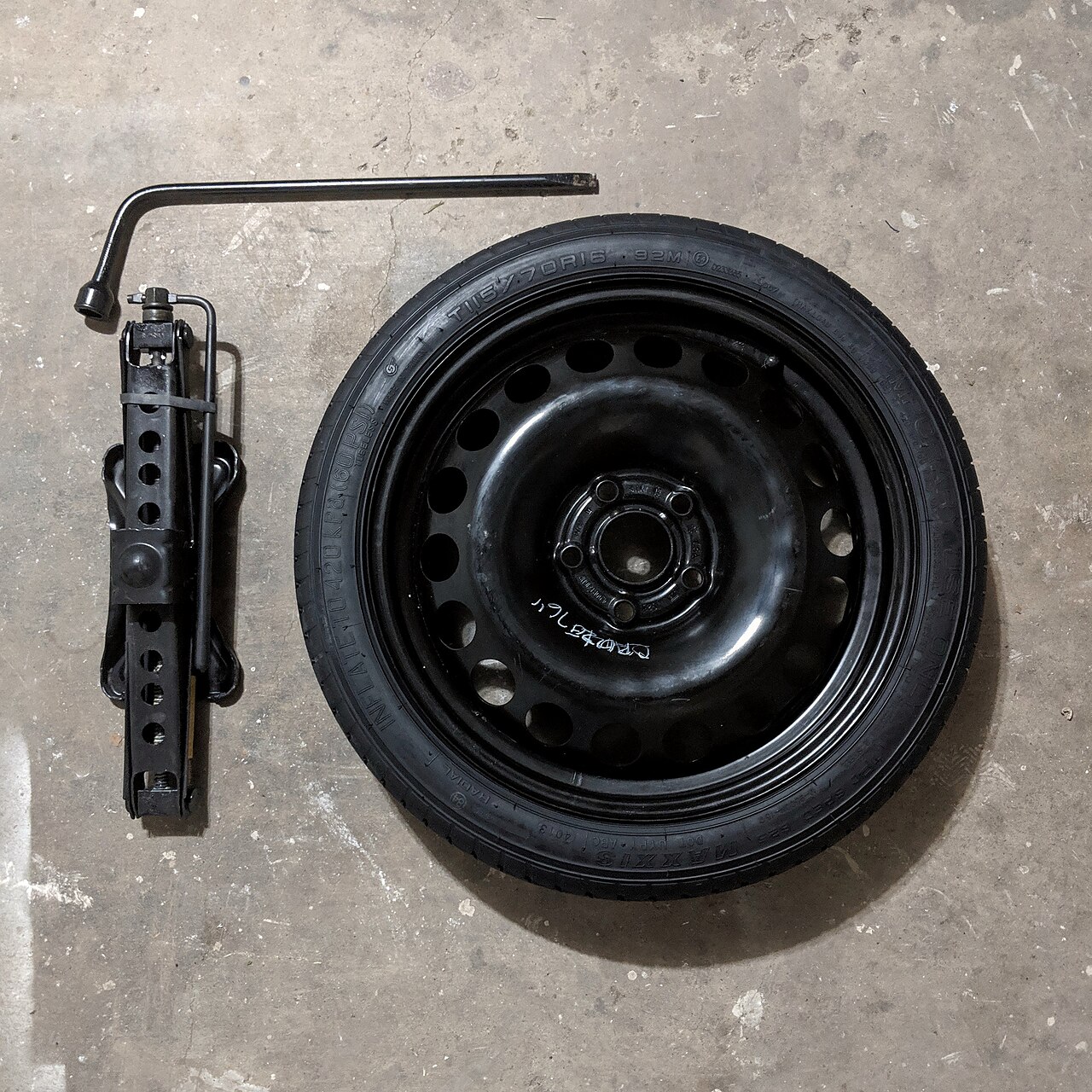 A spare tyre with a scissor jack and lug wrench laid out on the ground