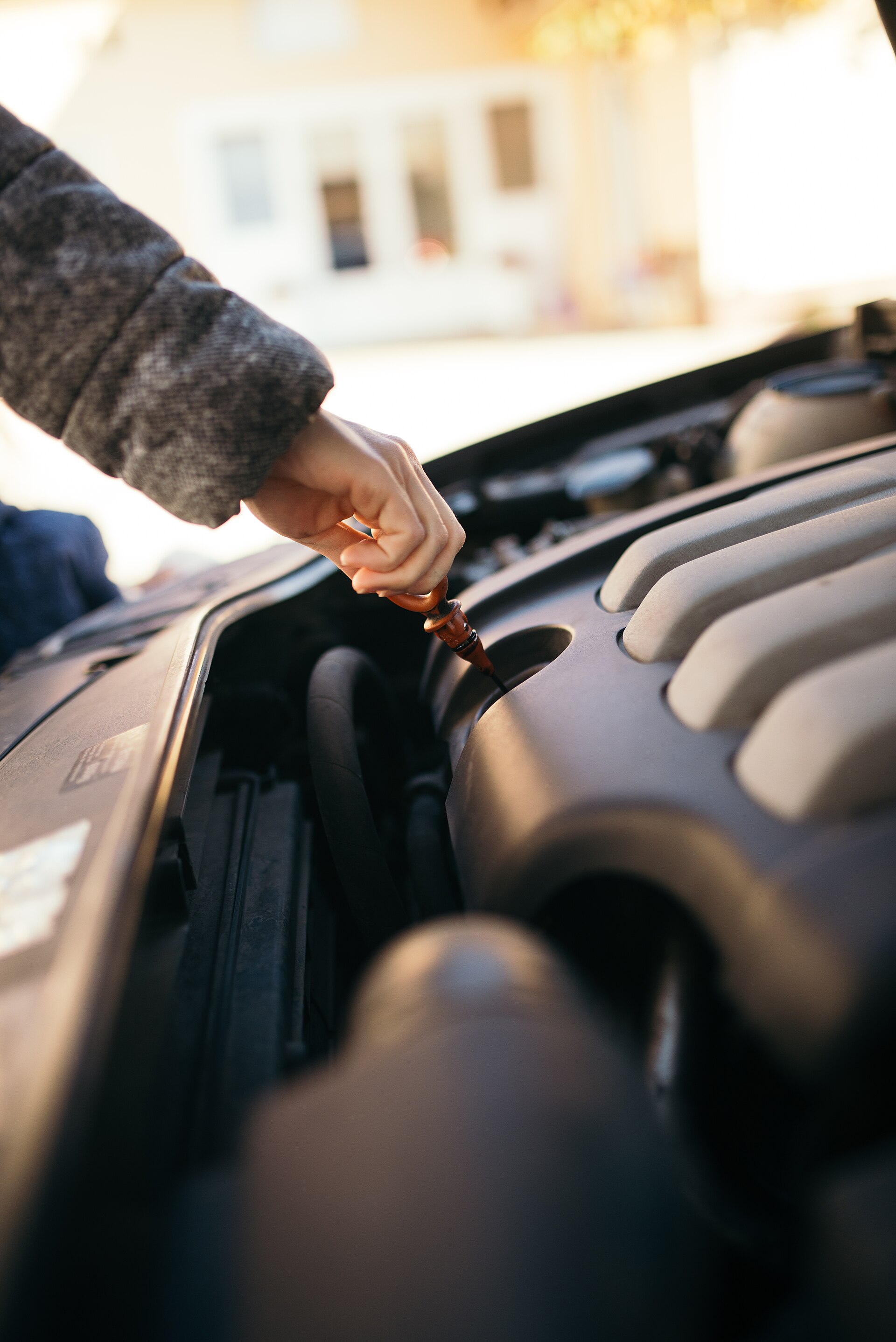 Person checking the engine oil level under the hood of a car in daylight
