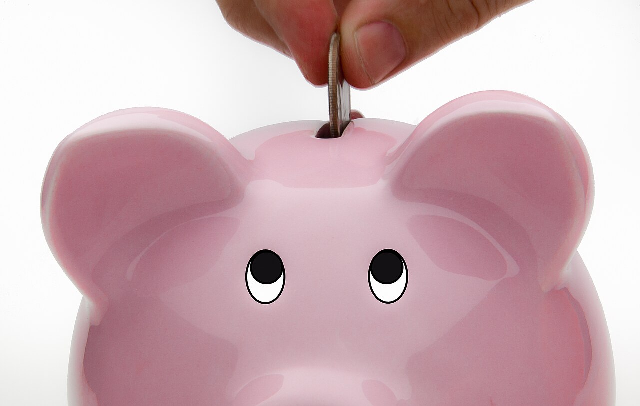 A hand drops a coin into a pink piggy bank