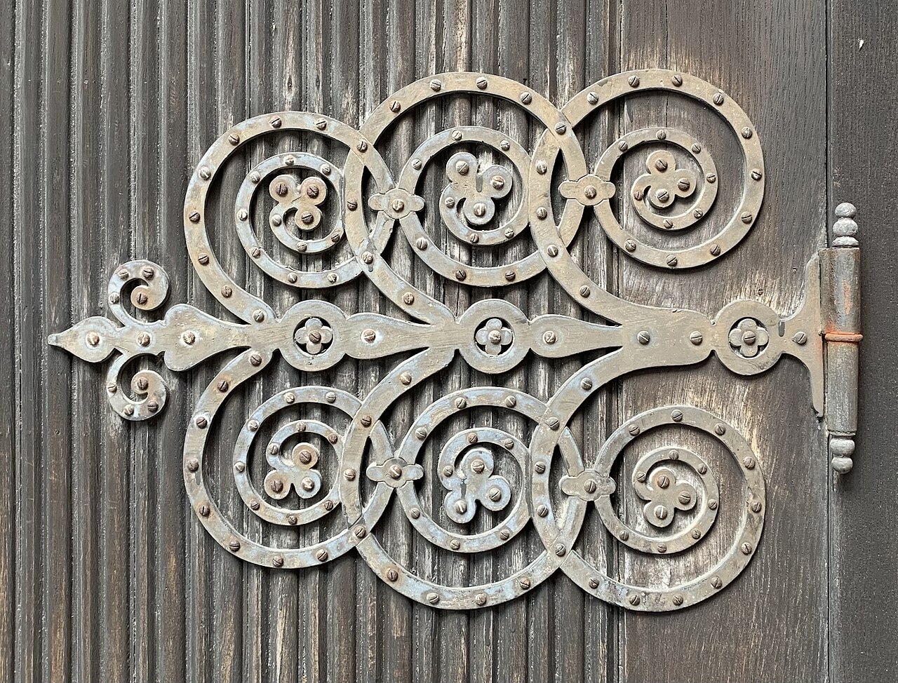 A decorative metal hinge on a wooden door