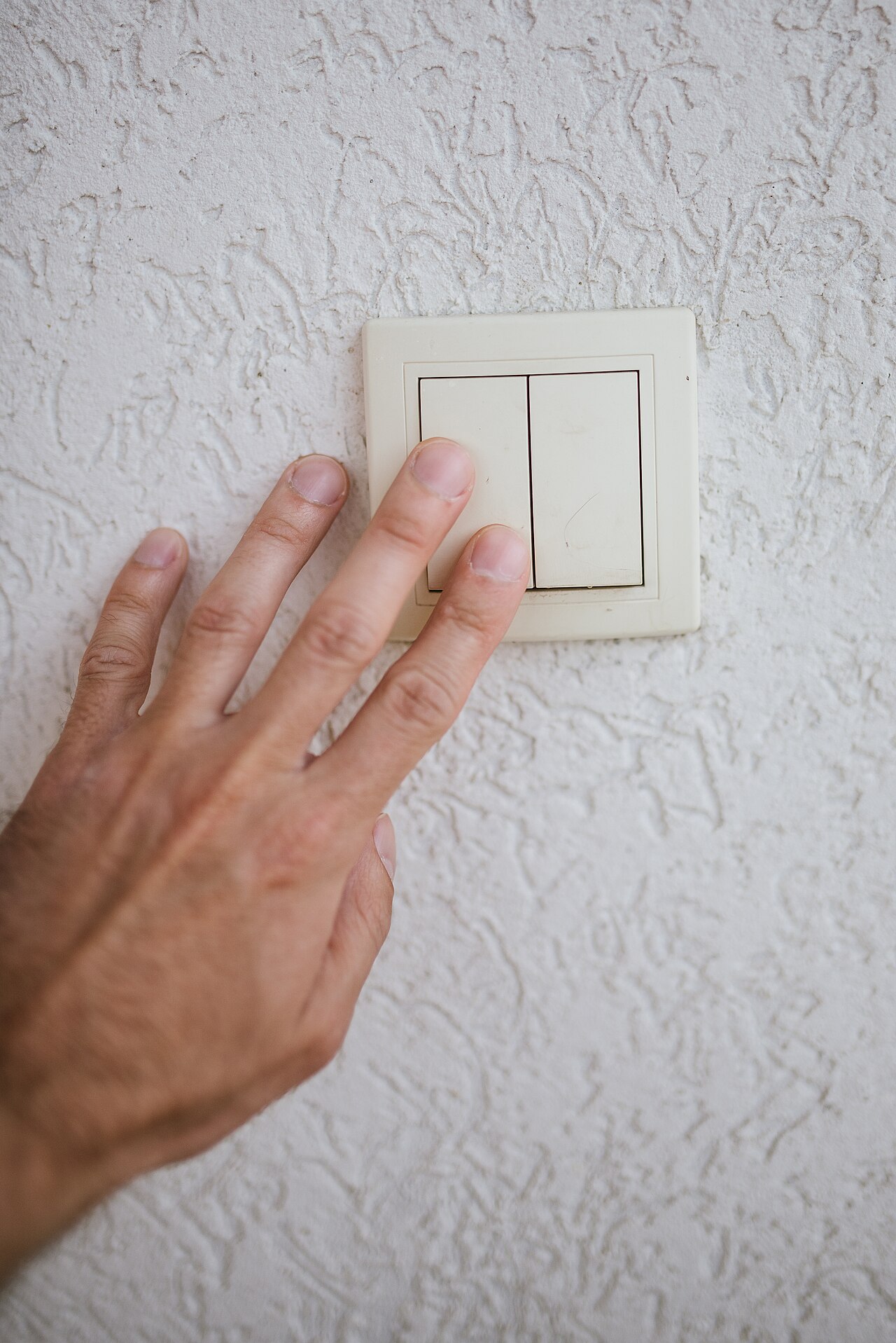 A hand reaching for a light switch on a textured wall