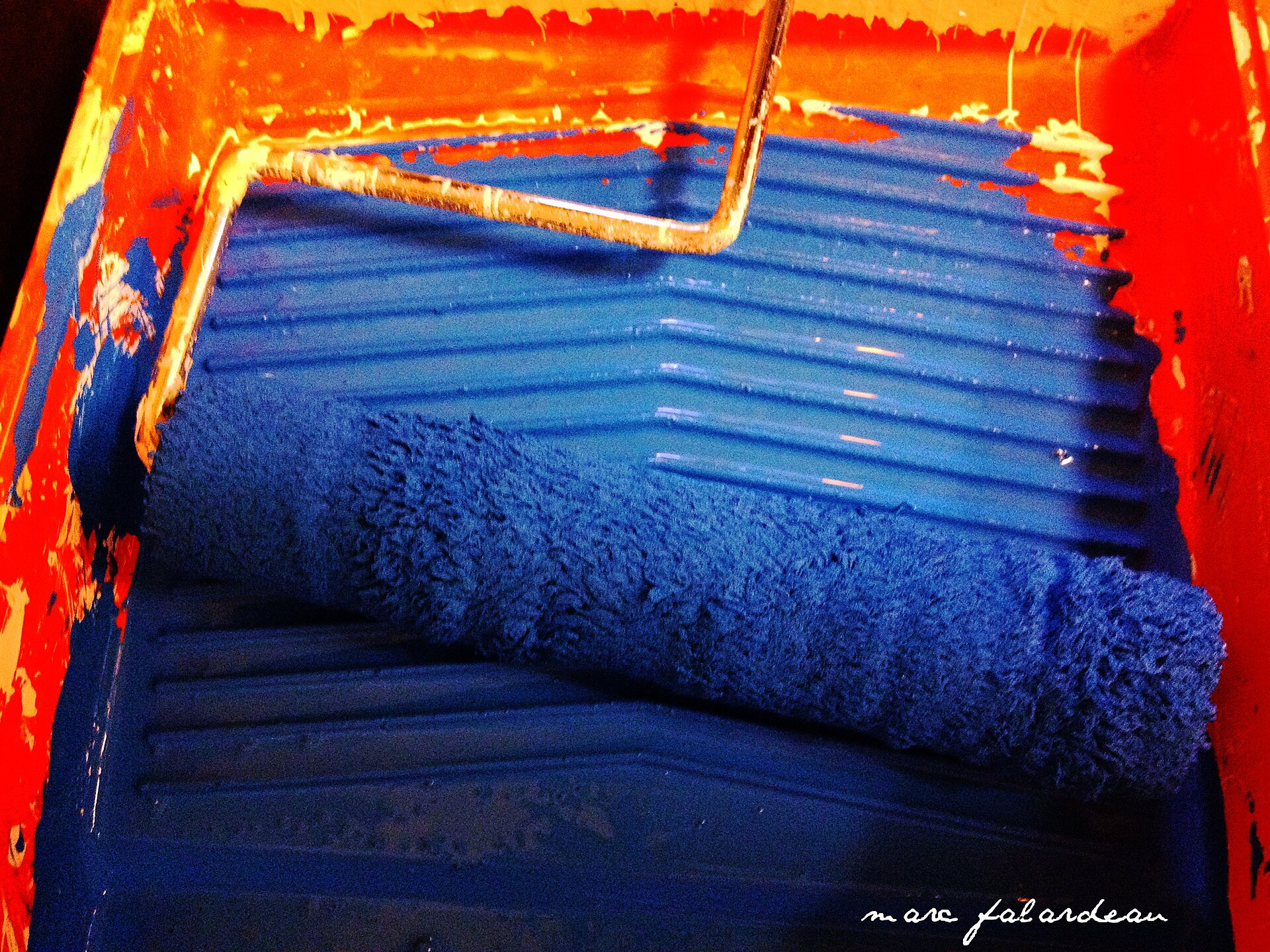 A blue paint roller resting in a paint tray