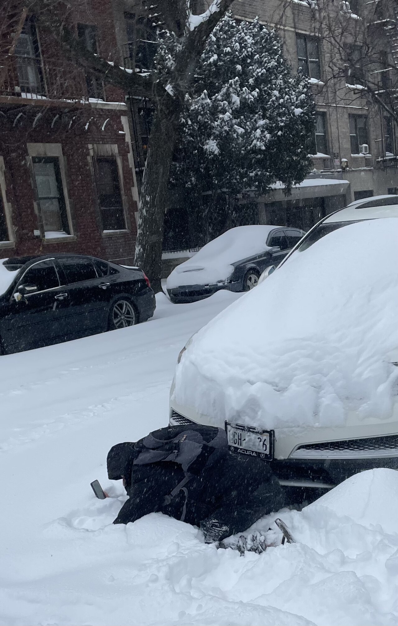 A person checks a phone while kneeling in deep snow next to a car