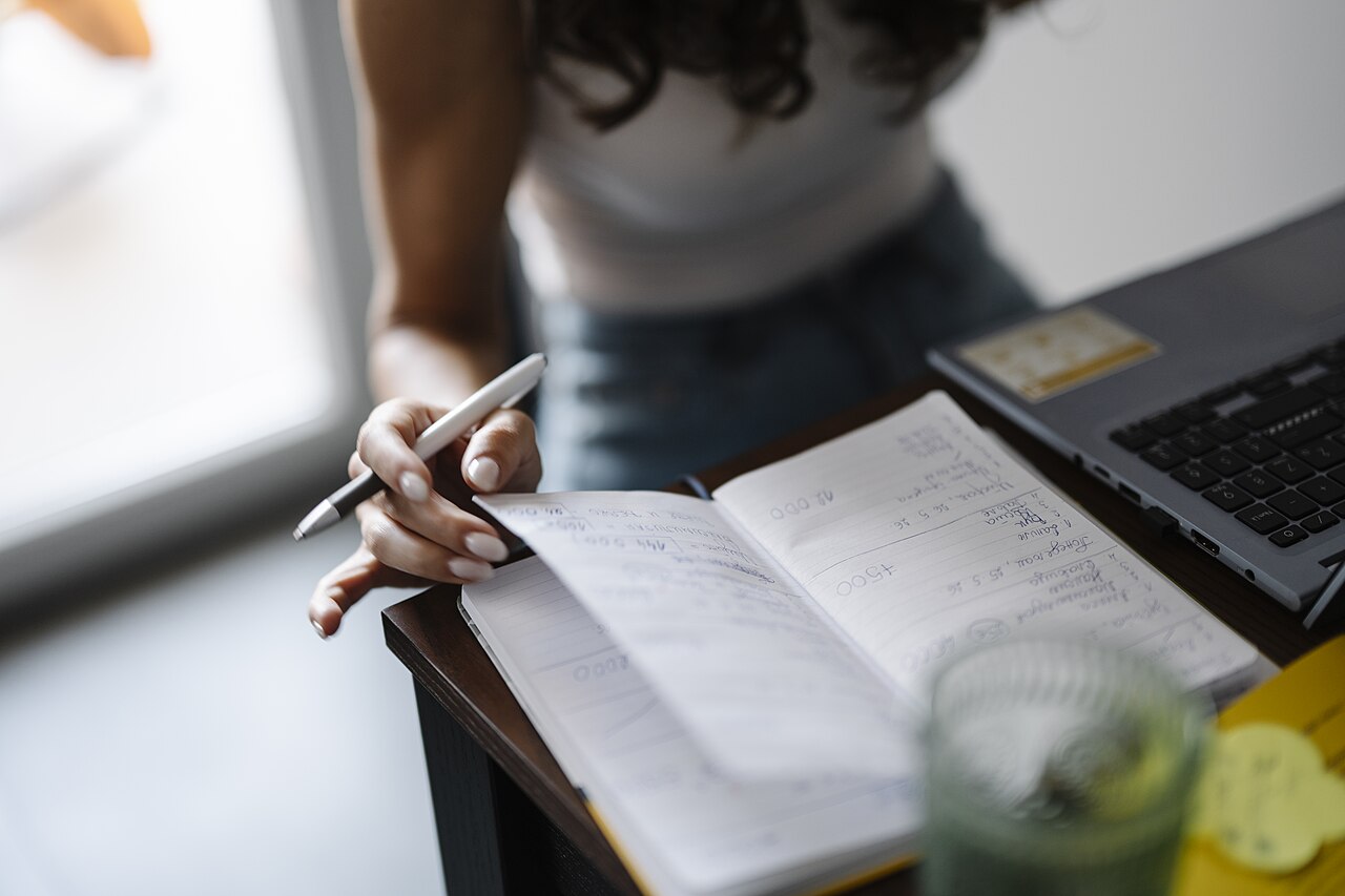 A person writing short bullet notes on paper at a desk