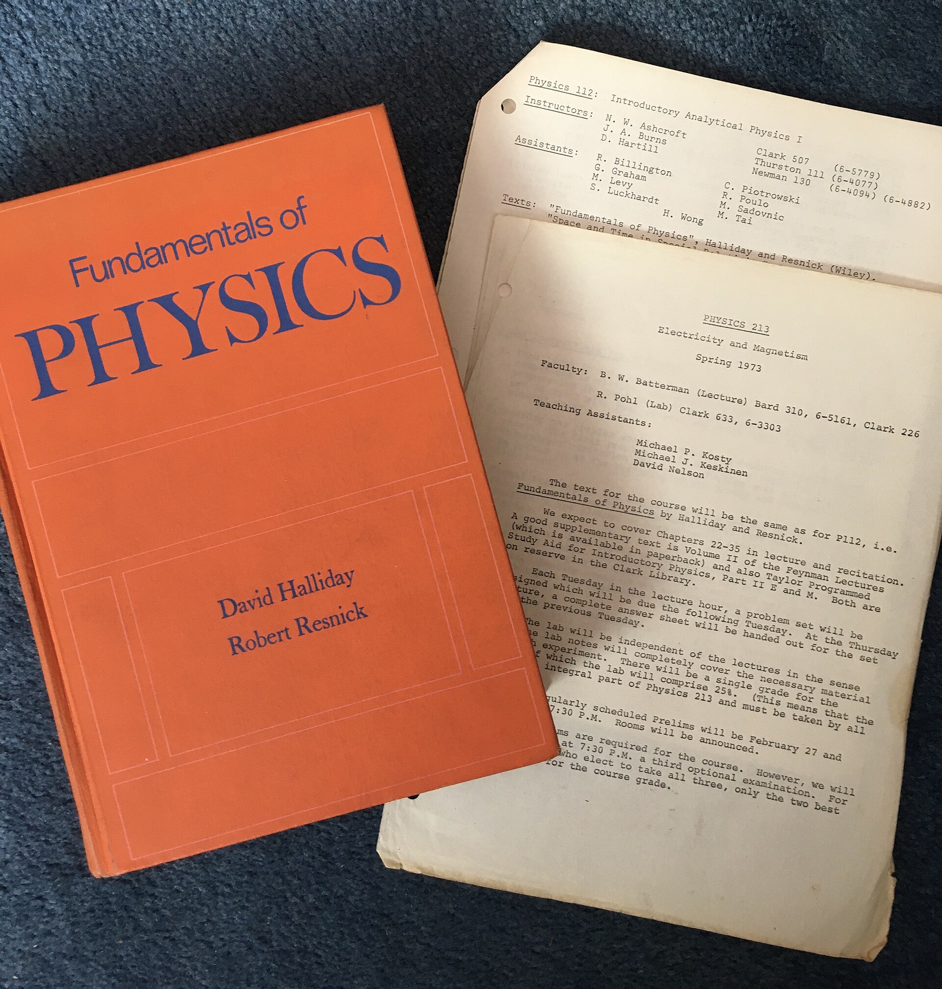 A physics textbook beside printed course syllabuses