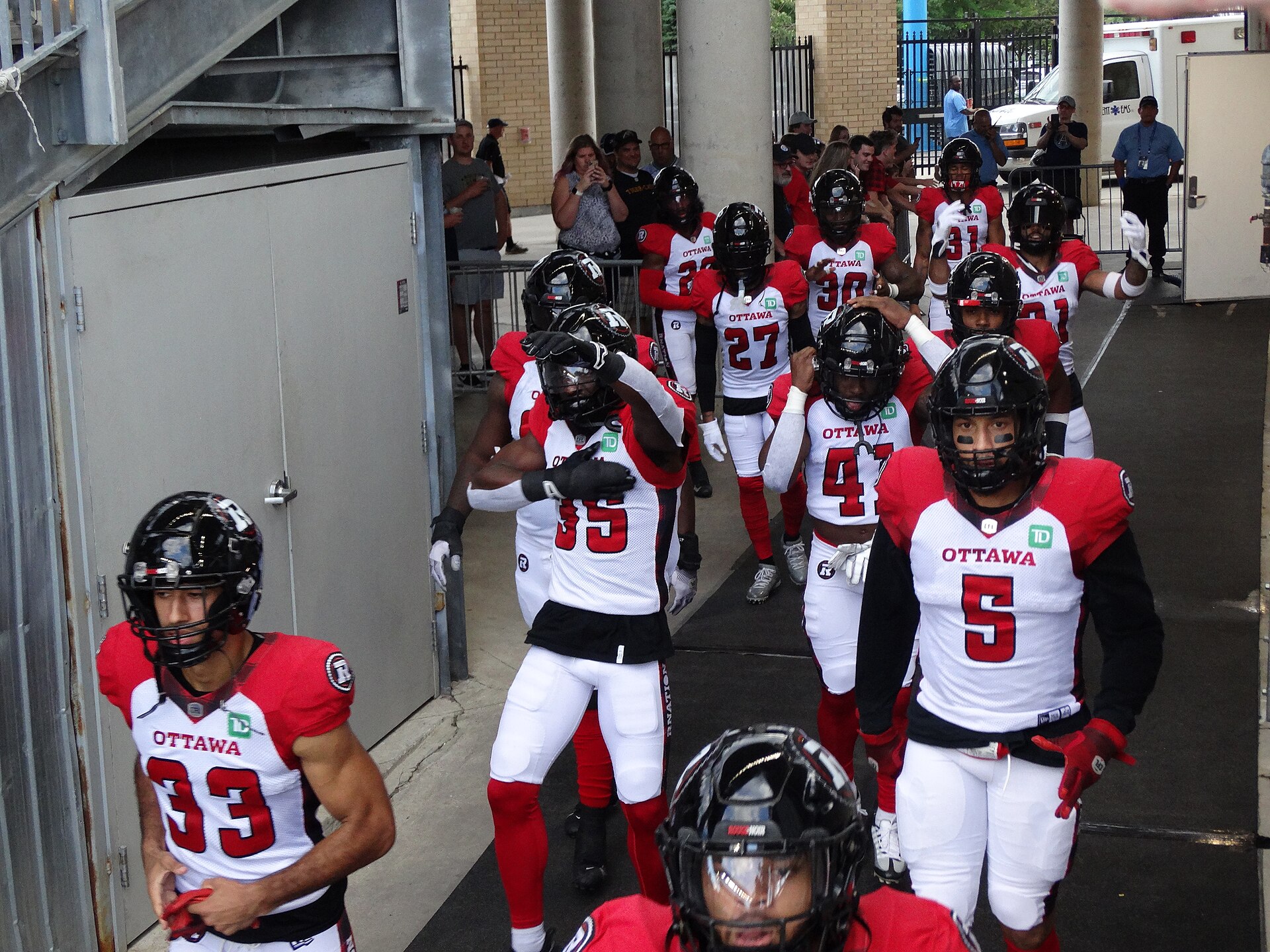 Ottawa Redblacks players in red and white walk out of the tunnel before a game