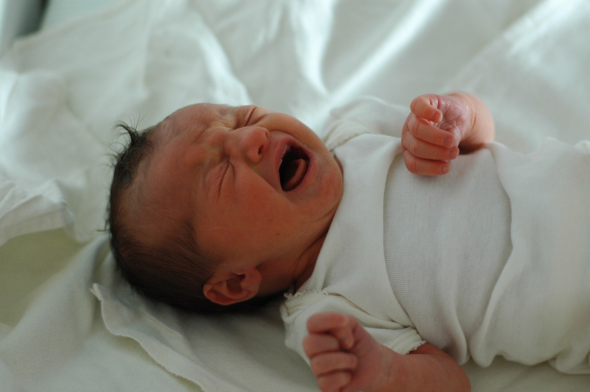 A newborn baby crying on white bedding