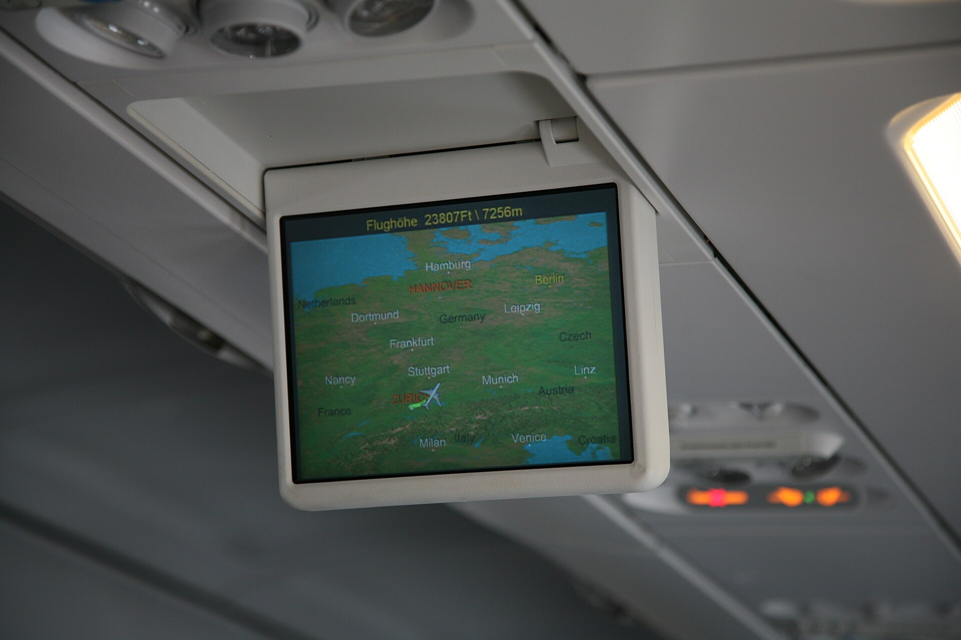 An overhead cabin screen shows a flight map over Europe