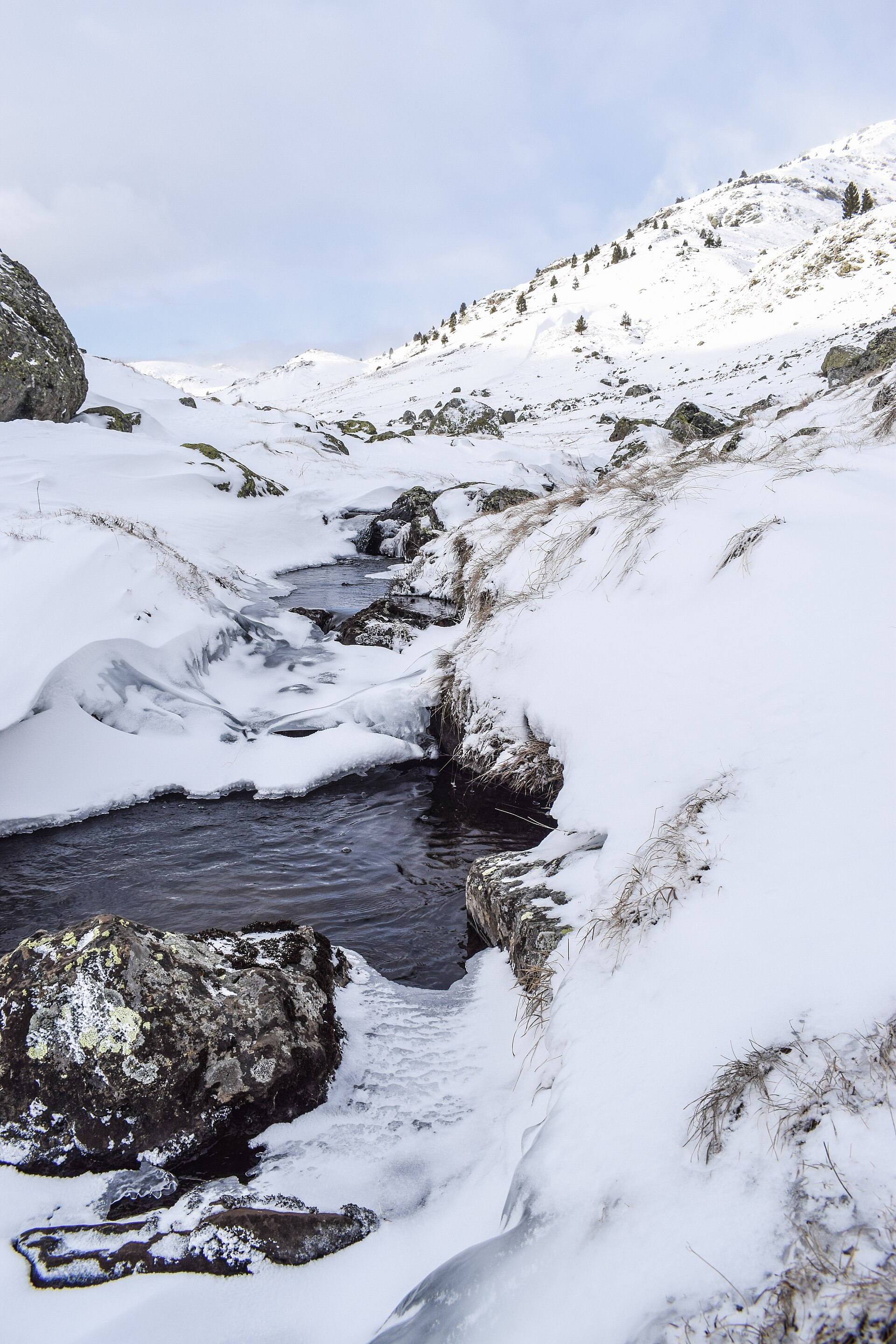 A partly frozen stream running through a snow-covered mountain slope
