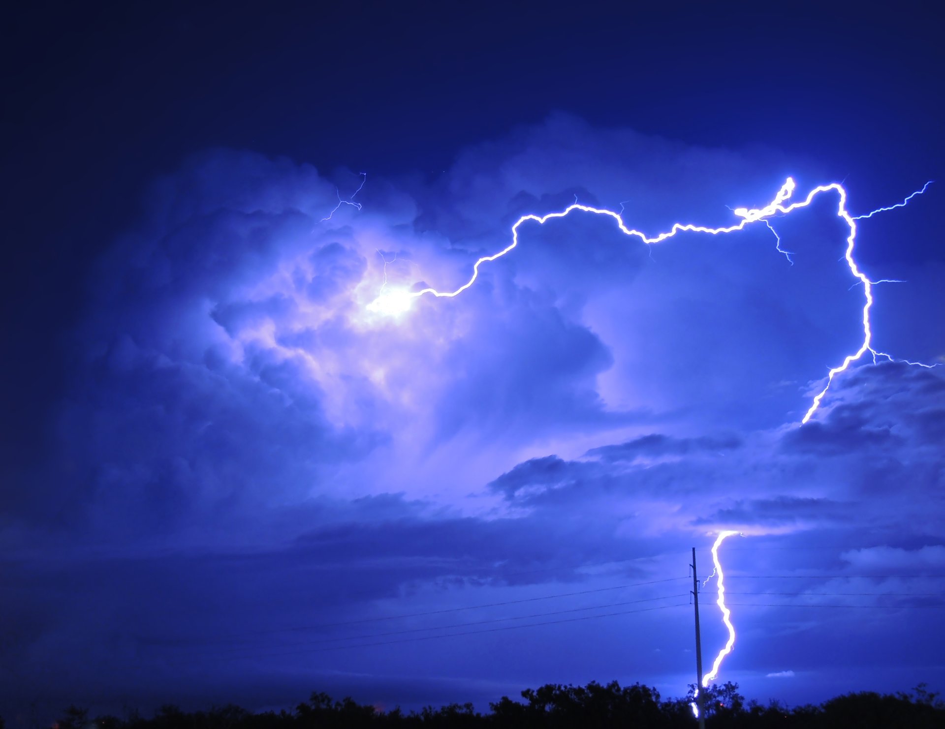 A lightning bolt forks across dark storm clouds over open fields