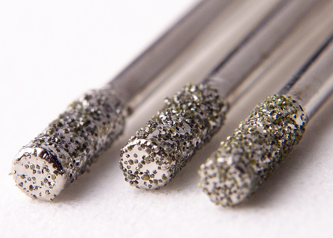 Close-up of three diamond-coated drill bits with grit-covered tips