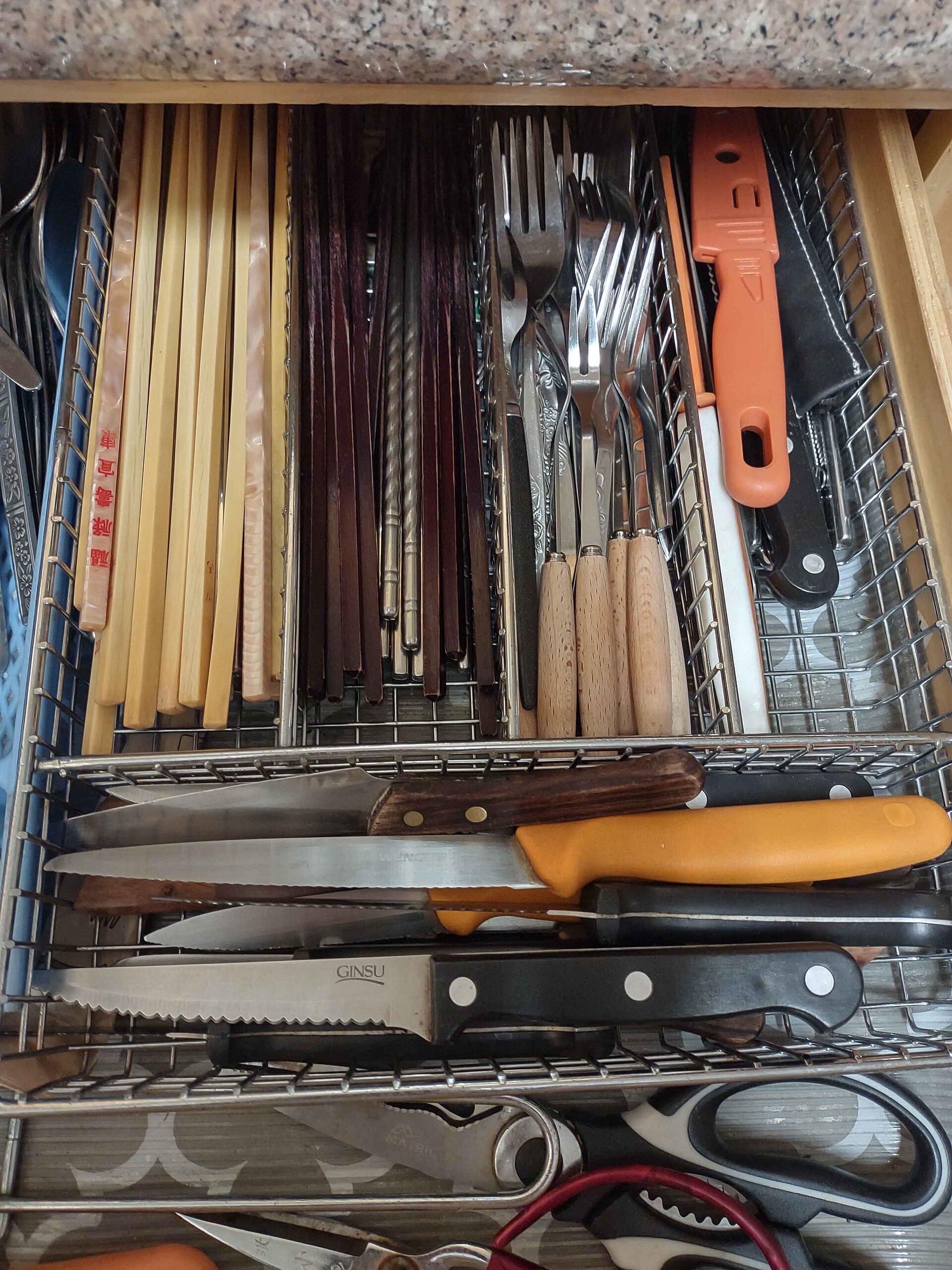 An open kitchen drawer full of cutlery in a wire organiser
