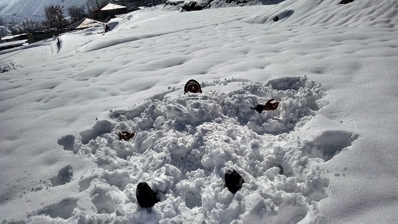 A person lying in deep snow on a sunny winter day