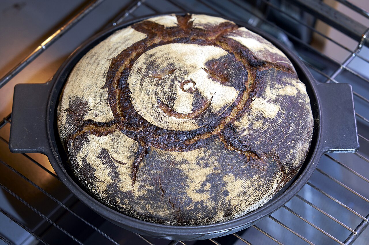 A round sourdough loaf baking in a Dutch oven on the oven rack