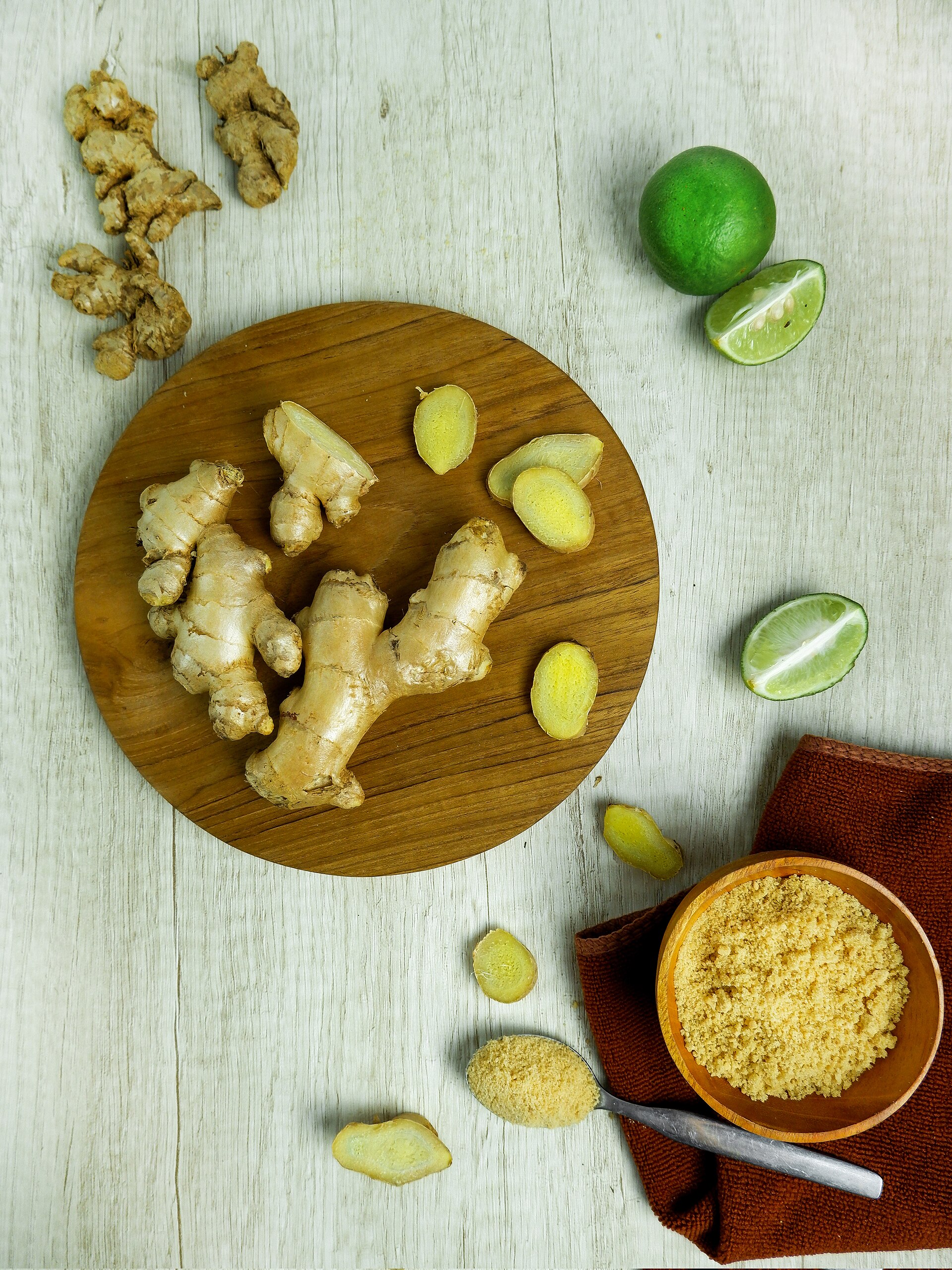 Sliced and whole ginger on a board beside lime and ground ginger