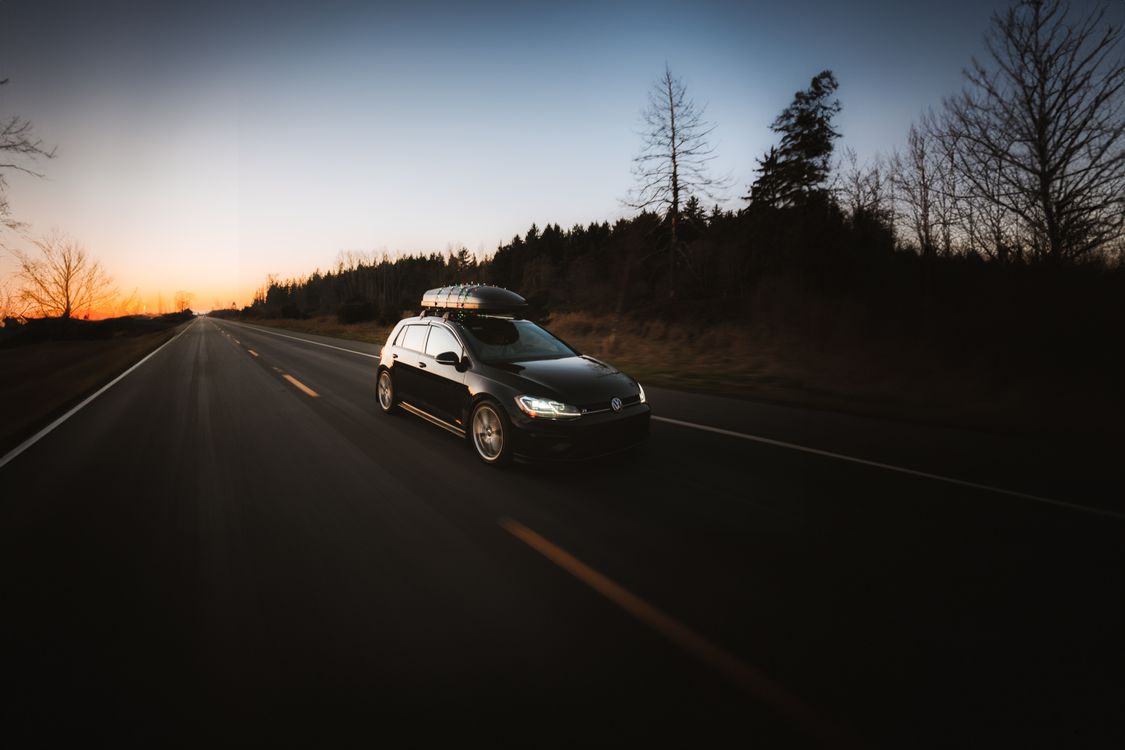 A car with a roof box driving on an open highway at sunset