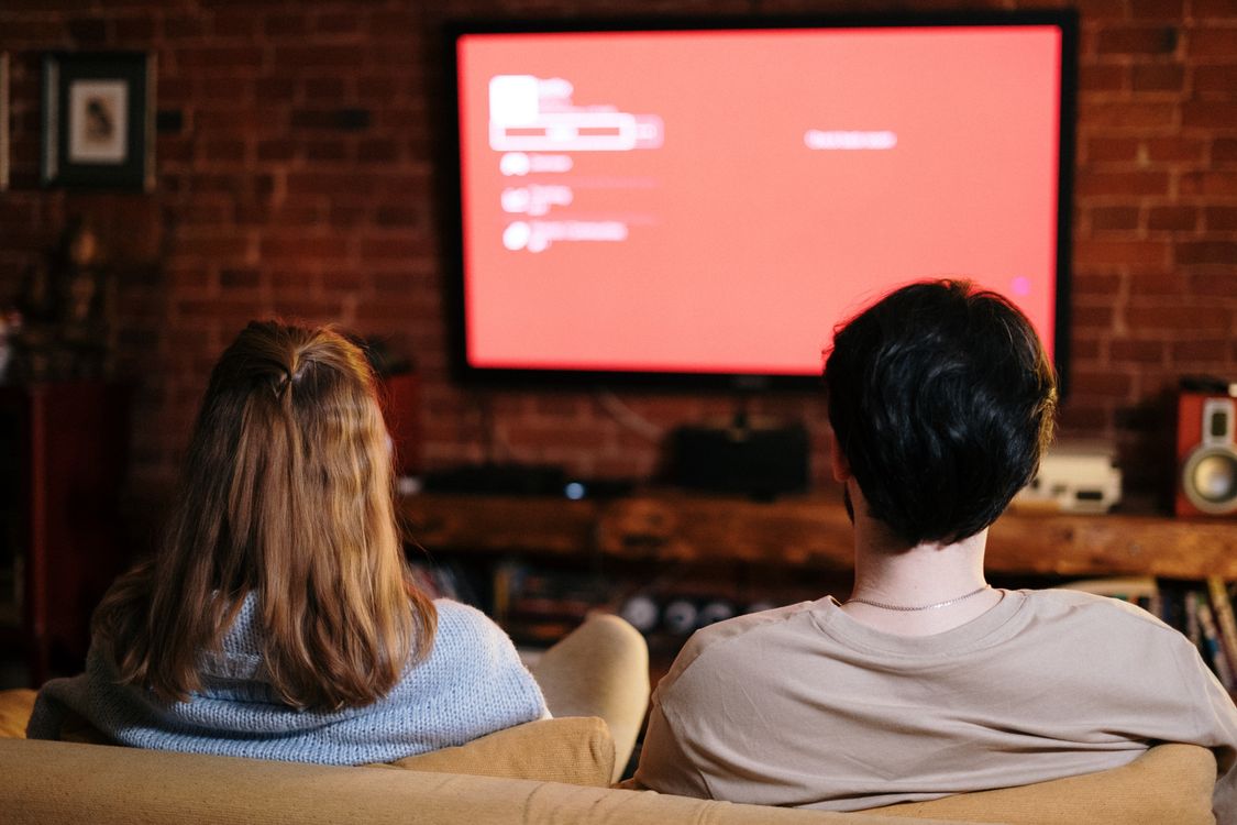 Two people watching a wall-mounted television in a living room