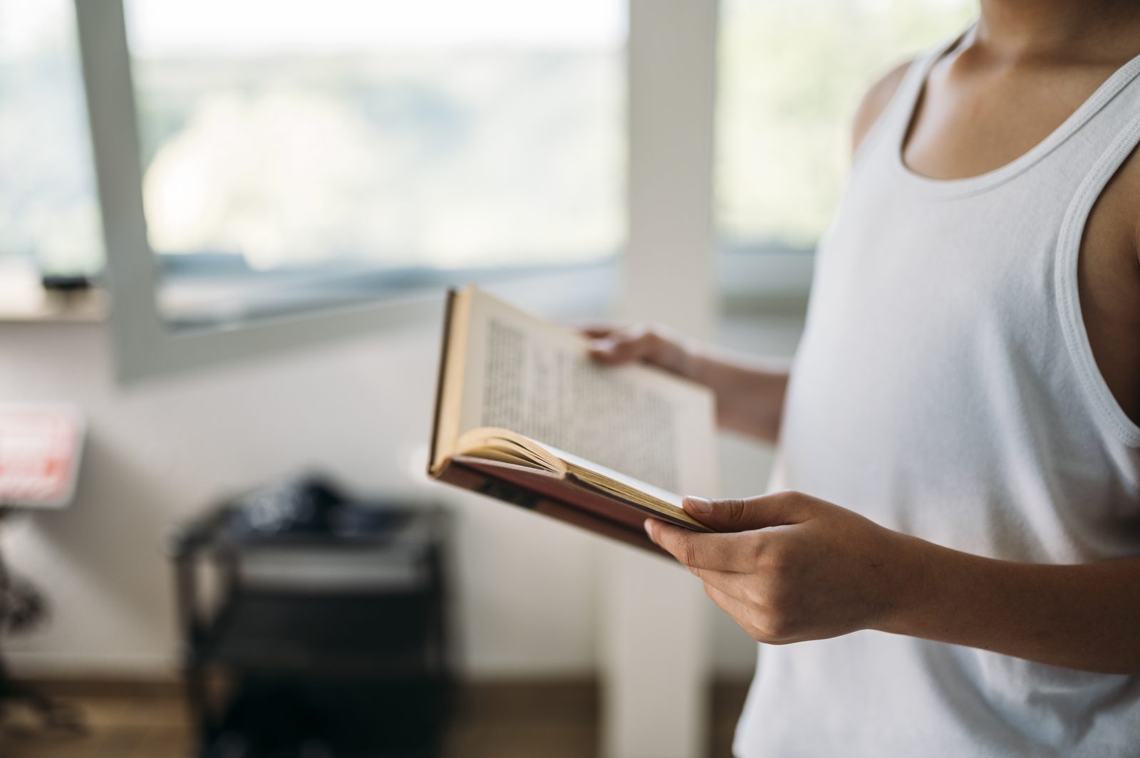A young person reading a book indoors in a light-filled room