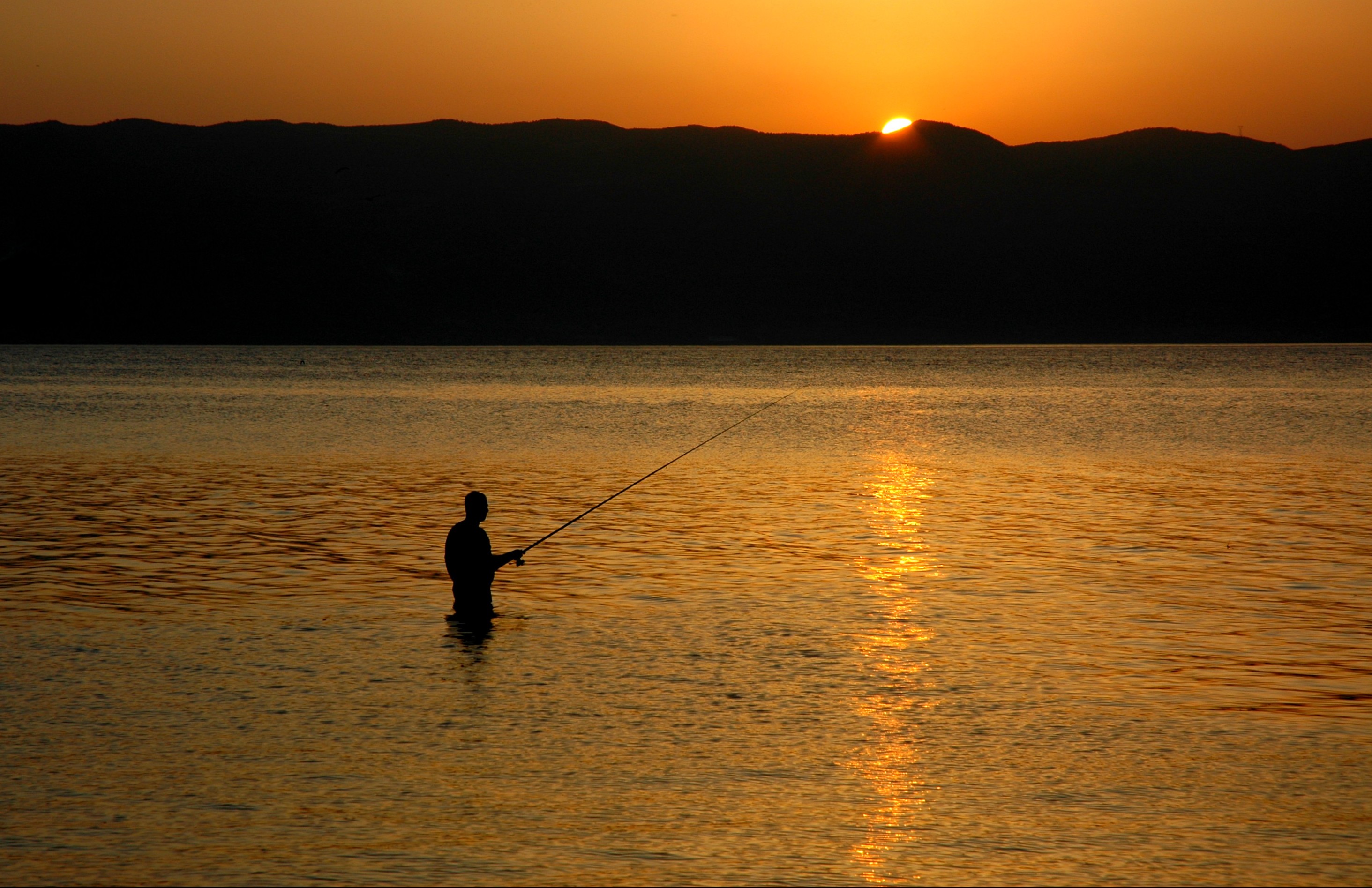 An angler fishing from the shallows of a lake at sunset