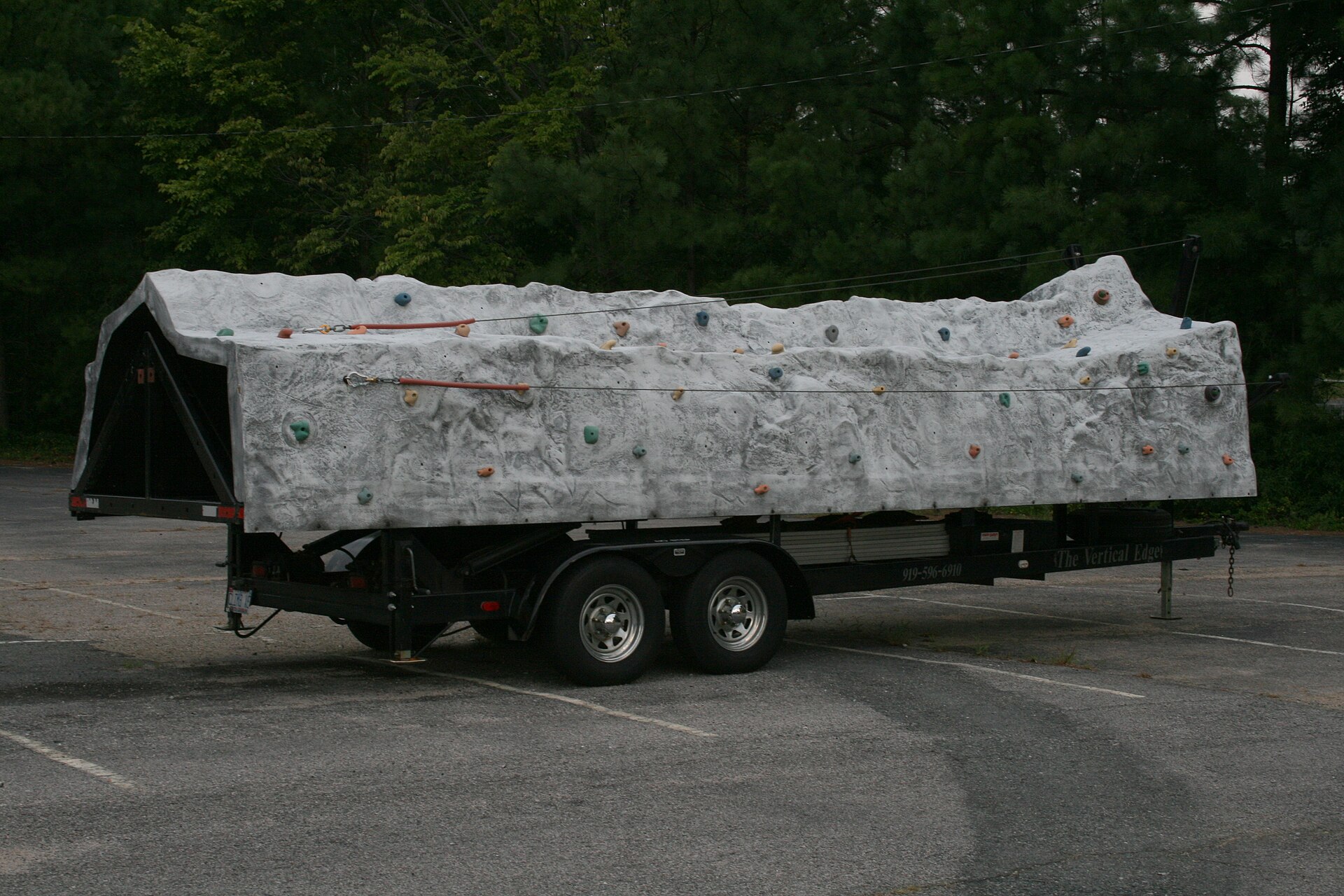 A portable climbing wall mounted on a trailer in a parking lot